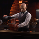 Hitman 3 a eu un mauvais lancement sur Steam, donc tout le monde obtient une mise à niveau 1 L'agent 47 verse un verre de malbec argentin dans une cave bordée de briques dans Hitman 3.